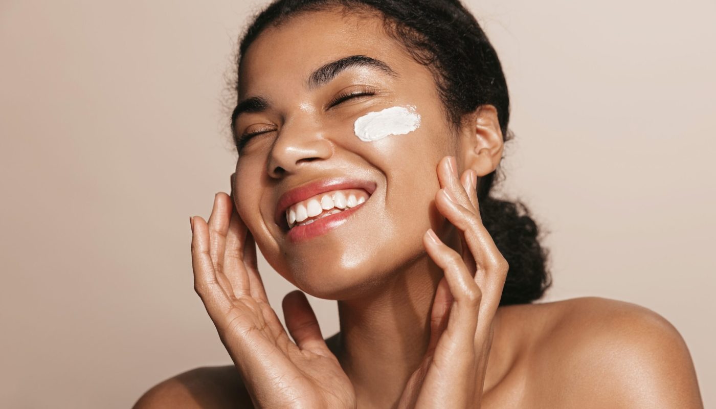 Smiling woman using skincare product. Female taking face cream to apply on facial skin.